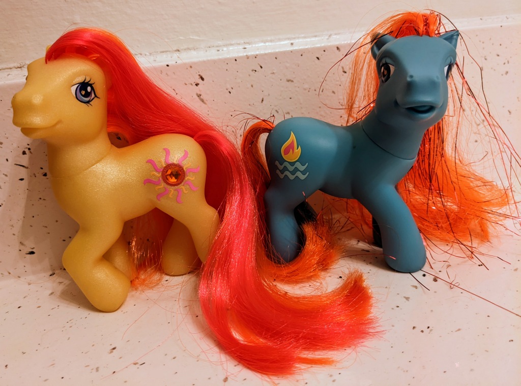 Sunshimmer is a yellow Earth pony with a red, neon orange and pink mane/tail, with a gemstone encrusted sun symbol for her cutie mark. Waterfire is a blue Earth pony with a bright orange/red mane/tail that has a ton of tinsel in it, along with a flame symbol with water lines beneath for her cutie mark. 